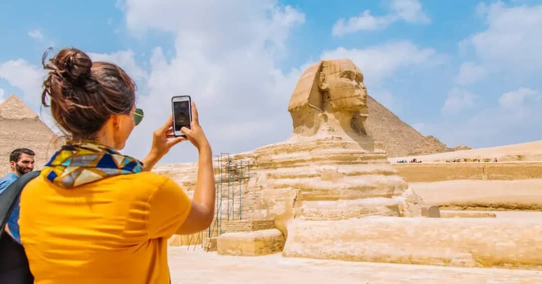 Una turista fotografía la Esfinge y las pirámides de Giza con su smartphone