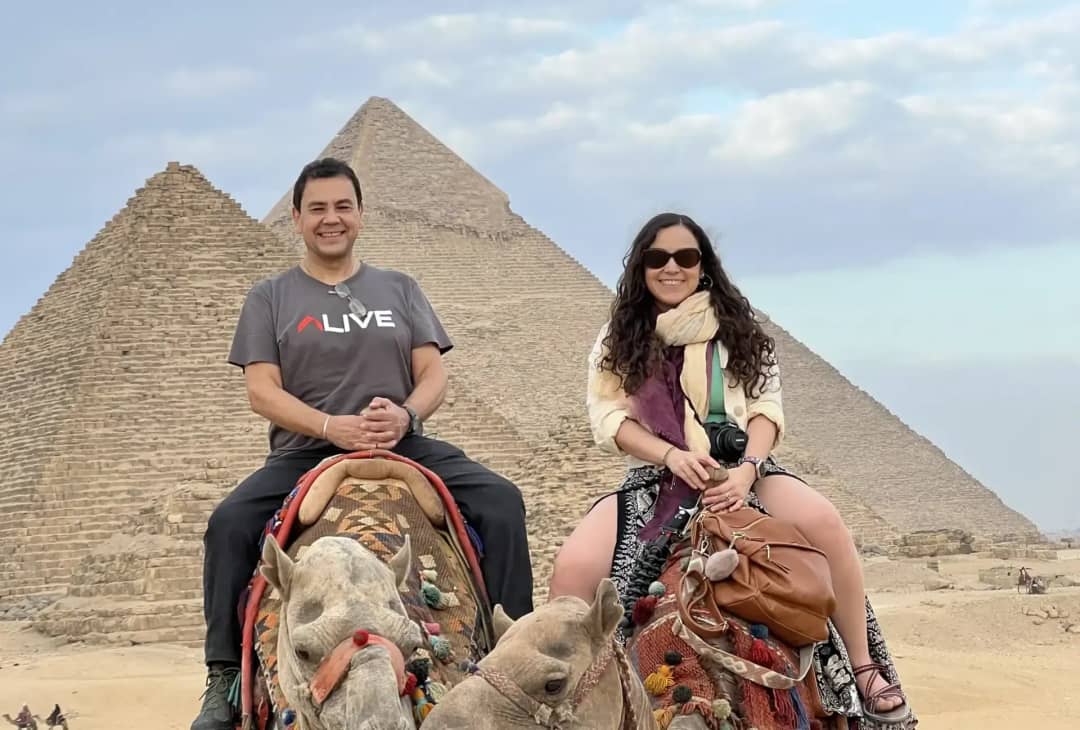 Pareja de turistas montando en camello frente a las pirámides de Giza, Egipto