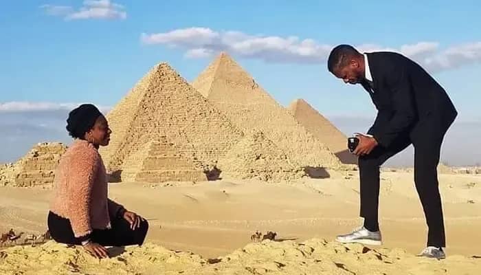 Hombre fotografiando a una mujer sentada en la arena frente a las pirámides de Giza