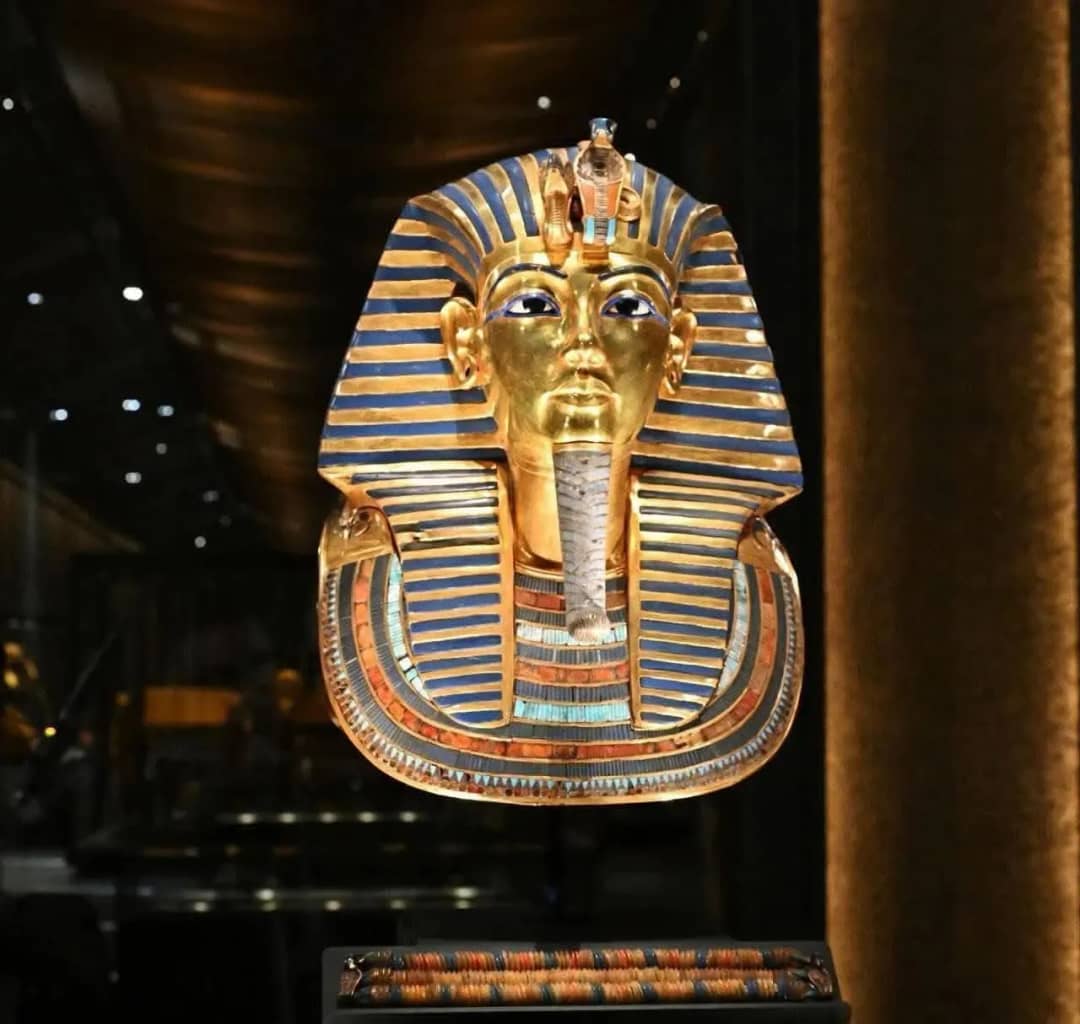 Máscara funeraria de oro de Tutankamón, con incrustaciones azules, expuesta sobre fondo oscuro en el Gran Museo Egipcio