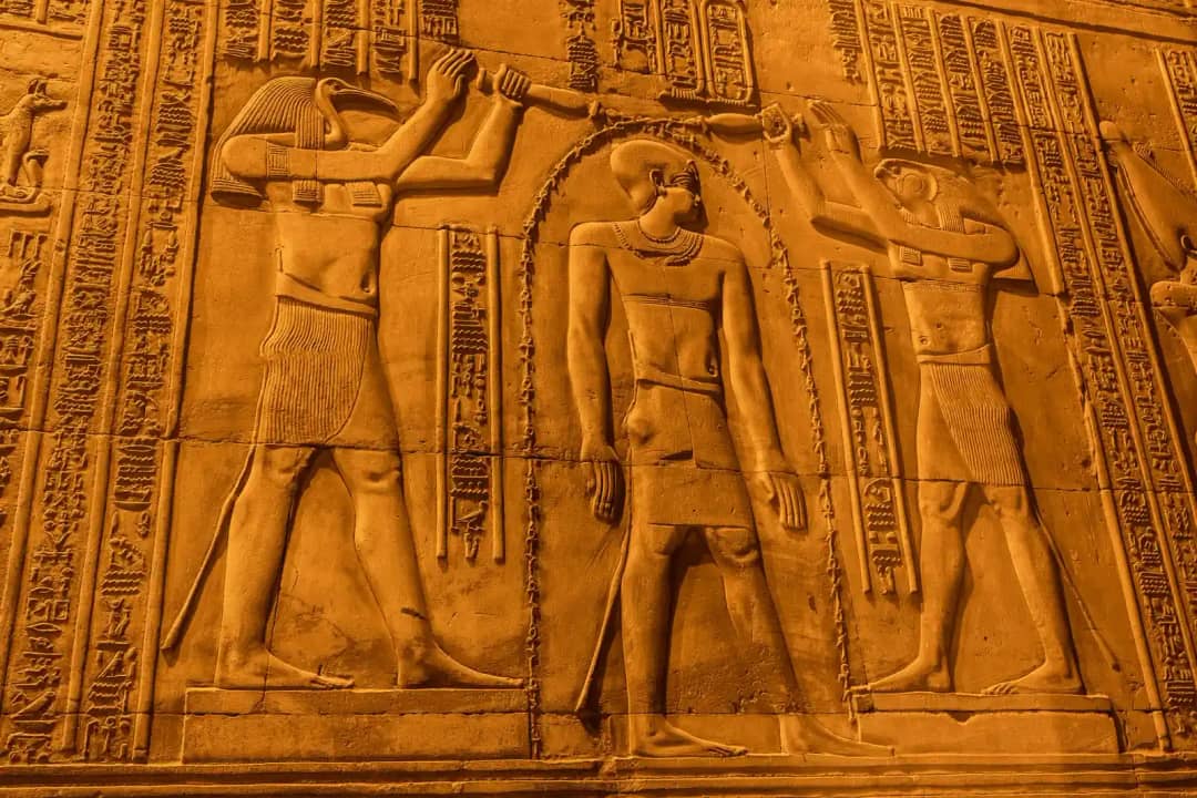 Relieve de un templo con una figura con cabeza de ibis y otra con cabeza de halcón que vierten un chorro de signos sobre un rey situado entre ambas