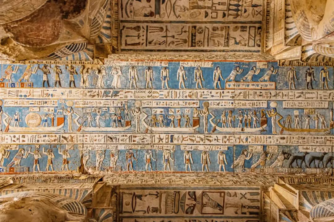 Painted temple ceiling with bands of hieroglyphs and rows of figures on a blue ground