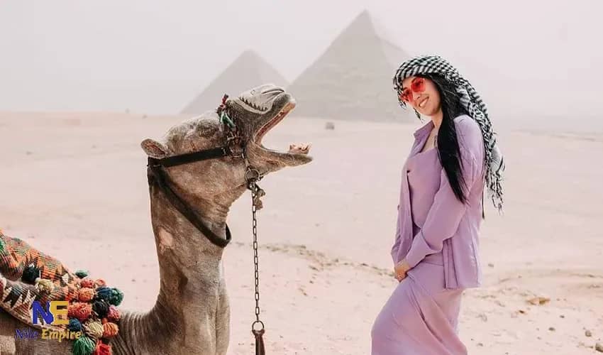 Viajera con pañuelo junto a un camello frente a las pirámides de Giza