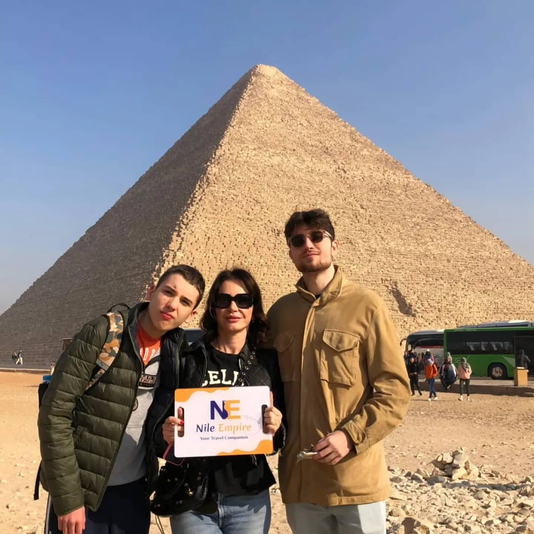 Three travelers holding a Nile Empire sign in front of the Great Pyramid